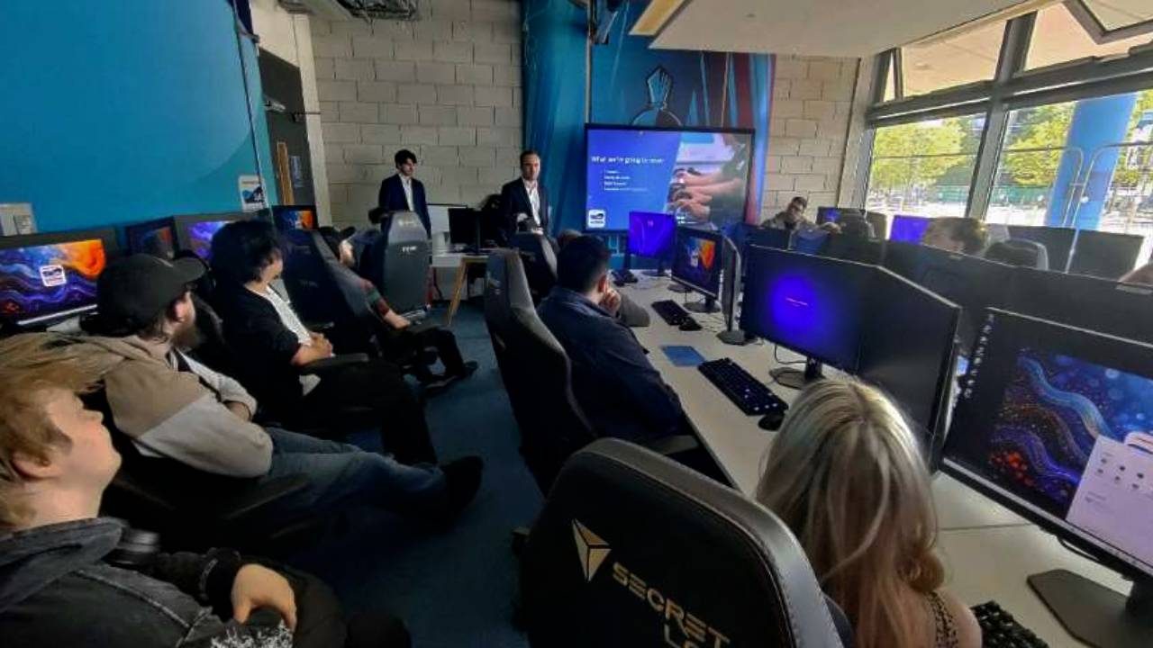Audience seated in College of eSports modern computer lab with branded chairs, watching a presentation titled 'The Future of...' displayed on a large screen at the front of the room.